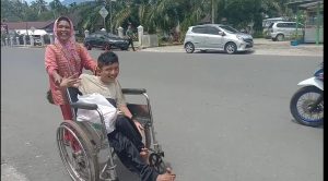 Foto : Sambil Mendorong Kursi Roda, Terlihat Senyum Bahagia Erni Bersama Anaknya yang Mendapatkan Kursi Roda di Simpang Empat, Kamis (06/08/2020) Siang