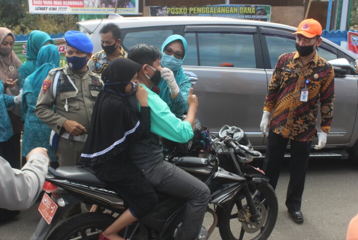 Keterangan Foto : Ketua PPK Pasaman Barat Ny Sifrowati Yulianto, SH Sedang Memasangkan Masker Kepada Pengendara Motor di Bundaran Simpang Empat