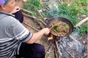 Salah seorang warga di Kecamatan Sumpur Kudus tengah memasak rendang belalang menggunakan kayu bakar